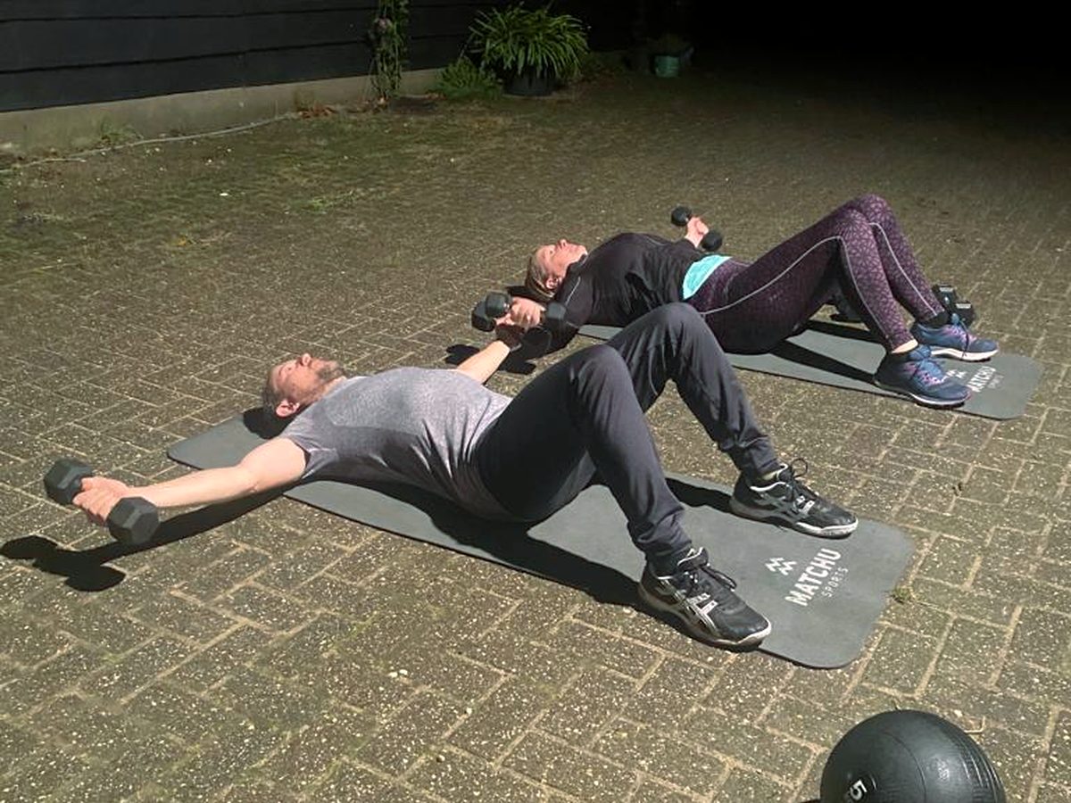 Drie mensen doen naast elkaar een liggende oefening met gewichten
