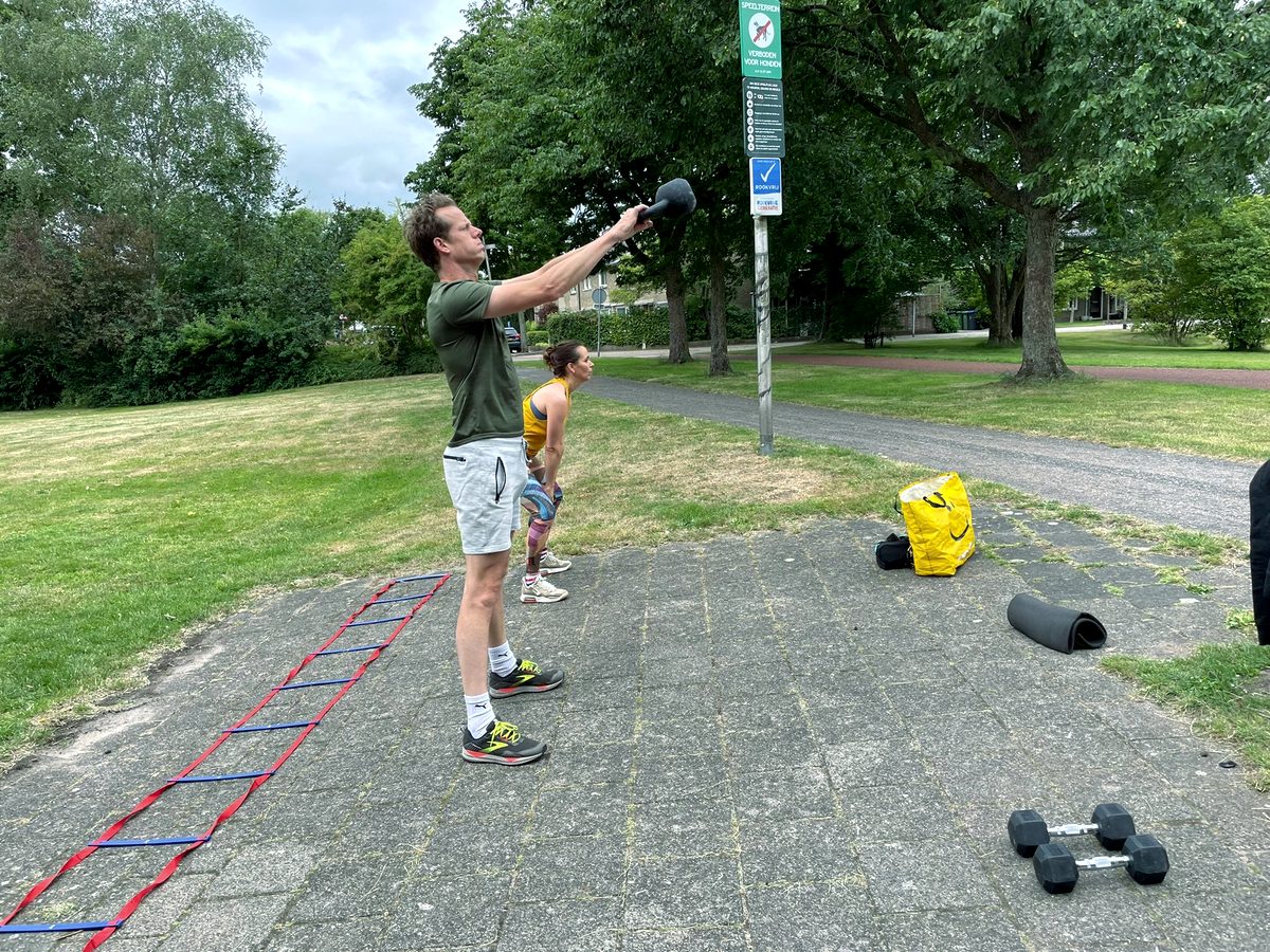 Twee mensen trainen met kettlebells op een pleintje