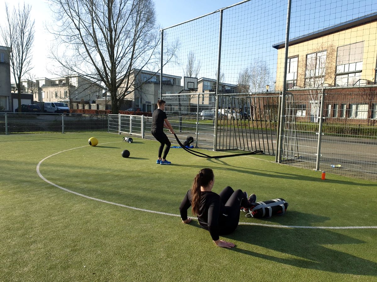 Twee mensen trainen op een kunstgrasveld bij een schoolgebouw
